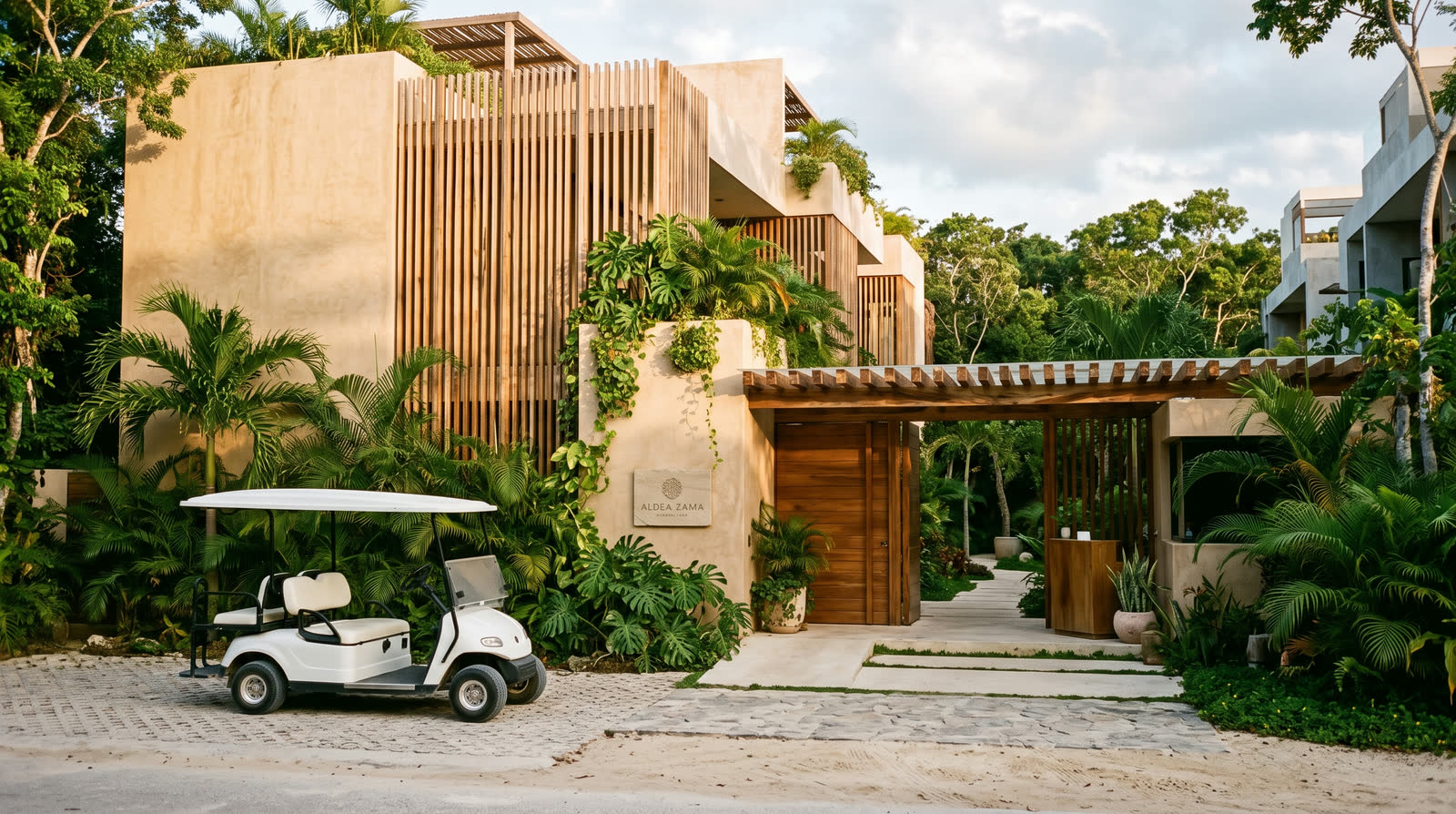 Carrito de golf blanco estacionado frente a la entrada de un edificio de departamentos en Aldea Zamá, Tulum